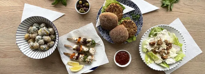 Table avec des assiettes : de pommes de terre, de la salade, des burgers végétariens à côté d'essuie-touts pliés et des brochettes posées sur un essuie-tout blanc.