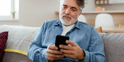 Homme âgé concentré sur son smartphone, assis sur un canapé.