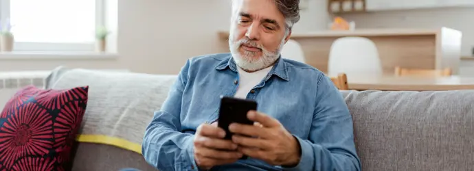 Homme âgé concentré sur son smartphone, assis sur un canapé.