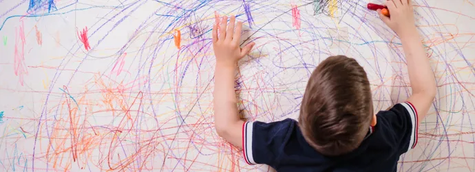 Enfant gribouillant sur un mur avec des crayons colorés