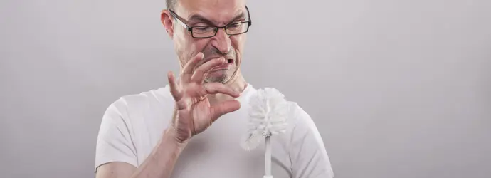 Homme tenant une brosse de toilettes avec l’air répugné