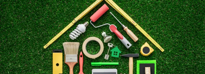 Divers outils de couleurs variées placés sur un sol en gazon, de sorte à former une maison.