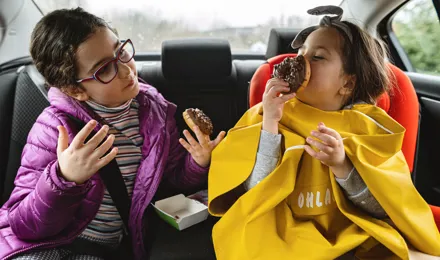 deux jeunes filles assises à l'arrière d'une voiture en train de manger des beignets