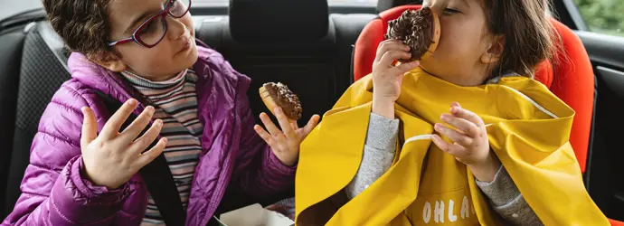 deux jeunes filles assises à l'arrière d'une voiture en train de manger des beignets