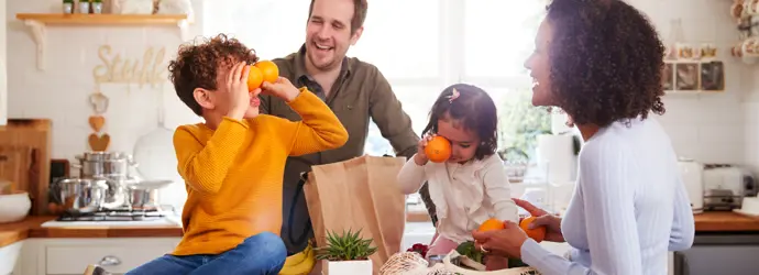 Deux enfants jouent avec des oranges ; des parents déballent leurs courses.