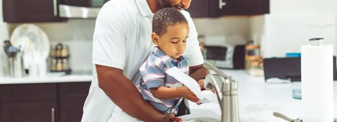 Un père se lave les mains avec son enfant à l'évier de la cuisine.