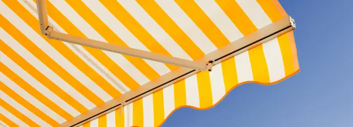 Stores bannes avec des rayures jaunes et blanches, vus d'en-dessous. On aperçoit un ciel bleu.